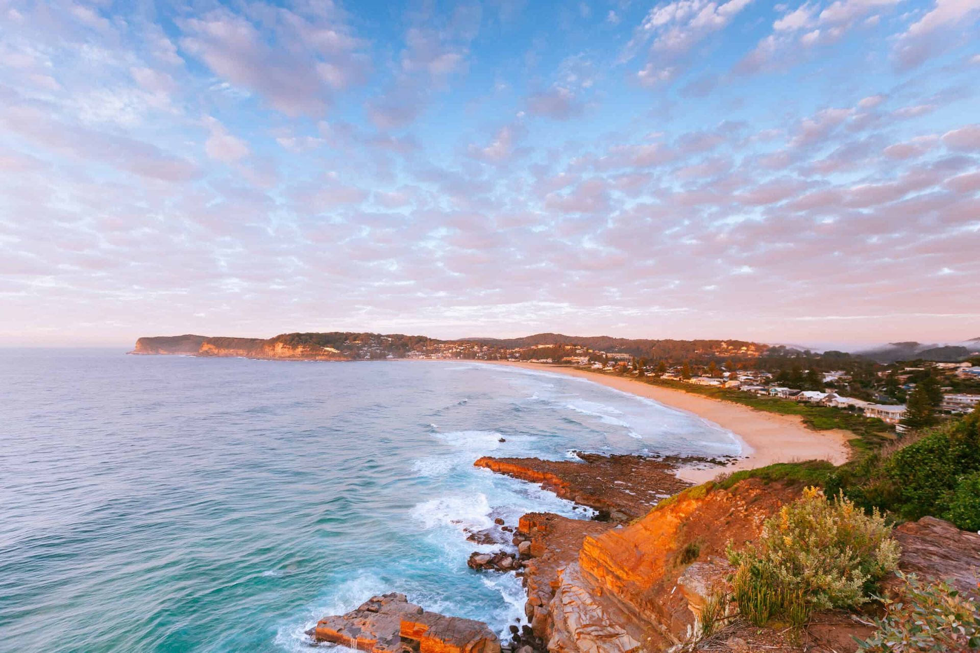 A view of a beach from a cliff overlooking the ocean at sunset.