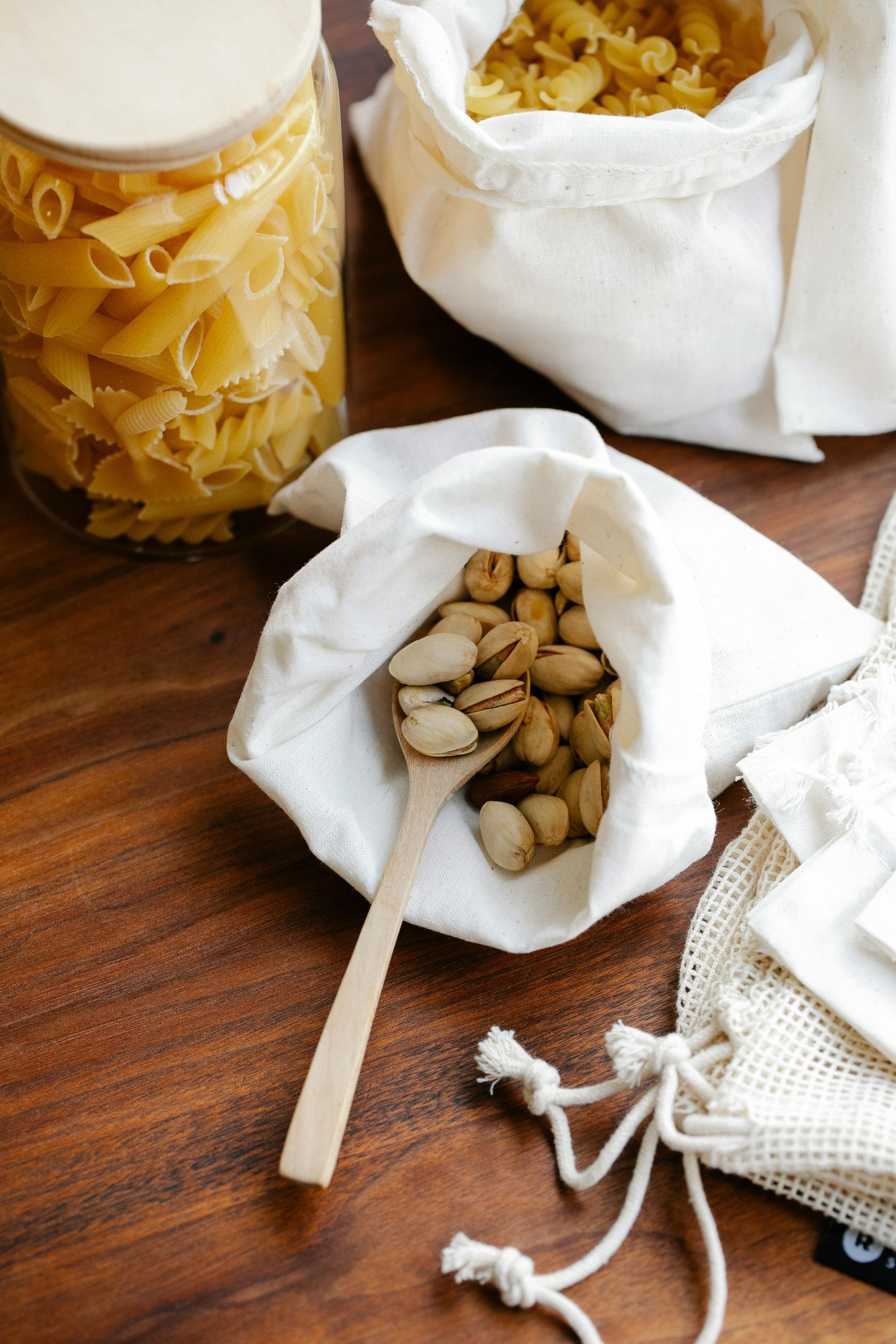 A wooden spoon is in a bag of nuts on a wooden table.