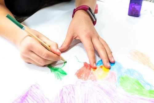 Hands drawing with colored pencils on white paper with rainbow scribbles