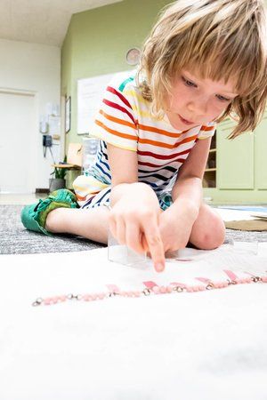 Montessori child kneeling on the floor, drawing with a red crayon in a bright room
