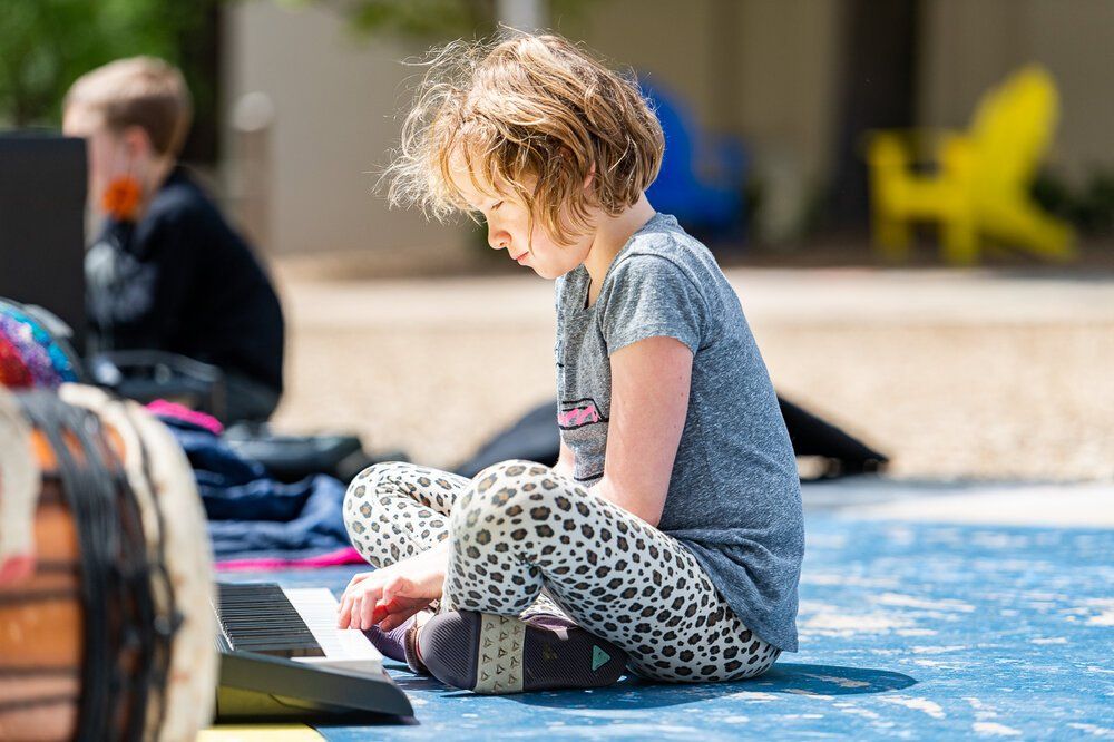 Montessori Child sitting cross-legged on a blue mat, using a laptop outdoors.