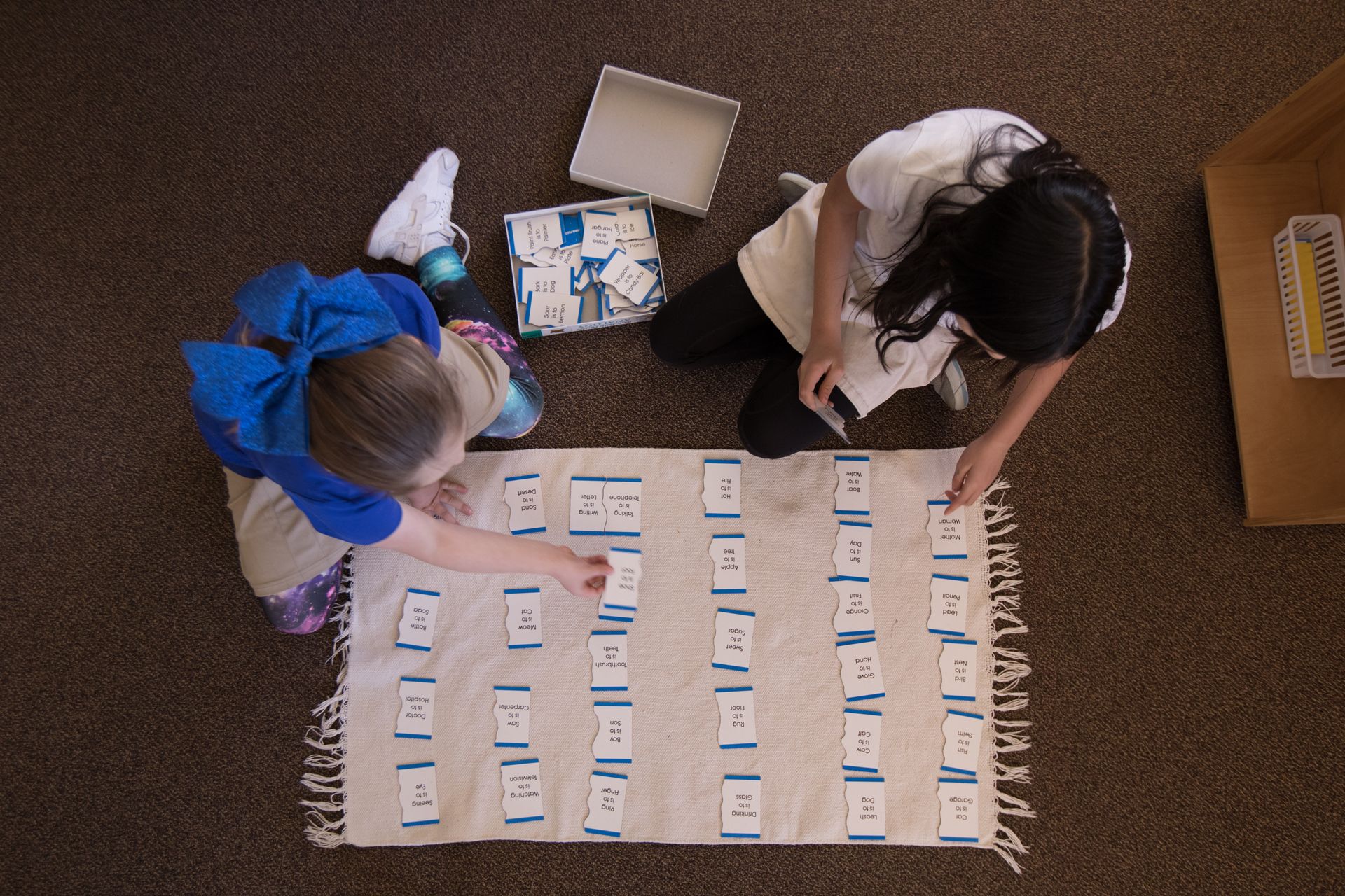 Two people sorting cards on a floor chart with rows of labeled notes and a box nearby