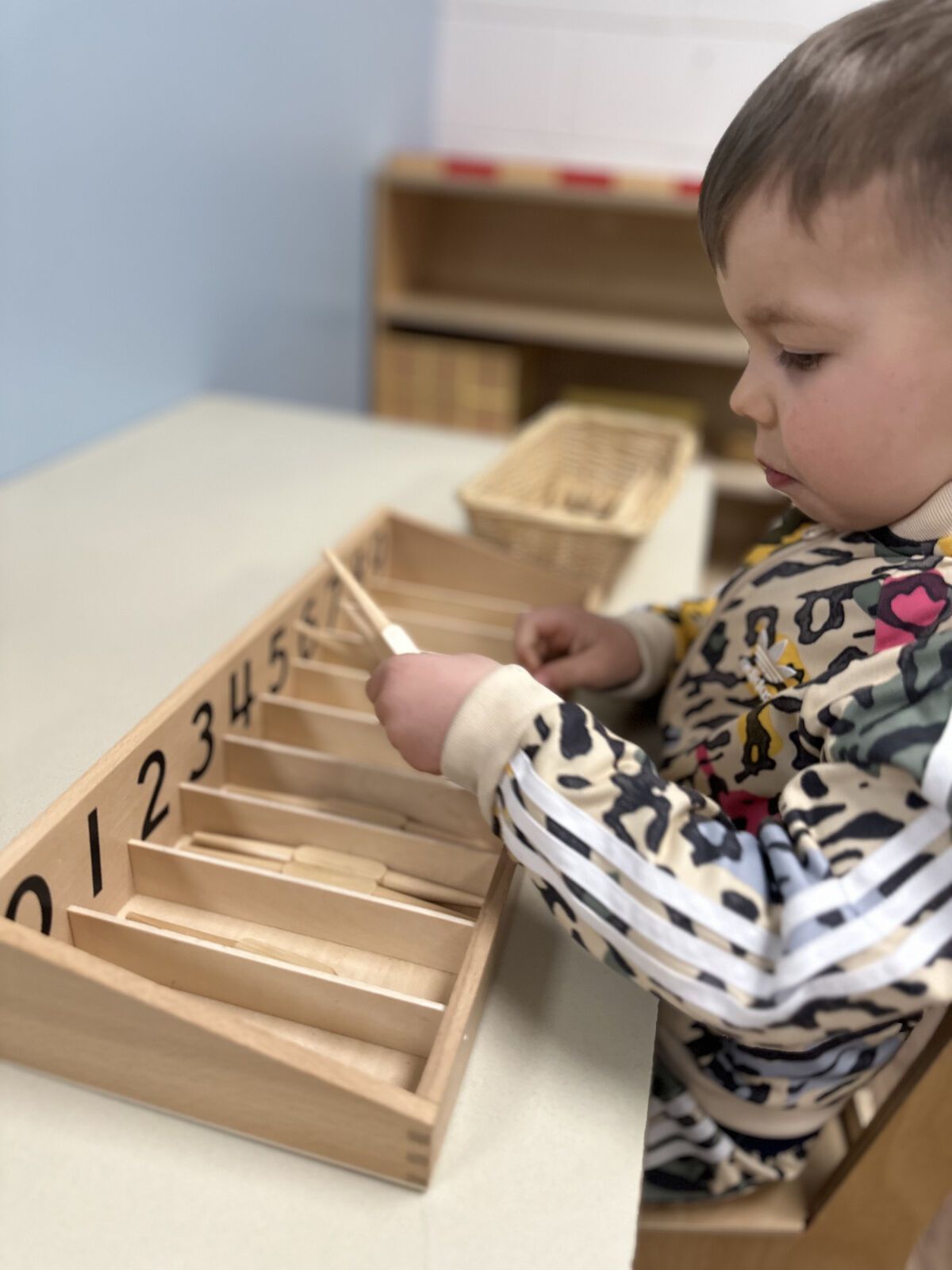 Child using a wooden counting toy at a table in a classroom.