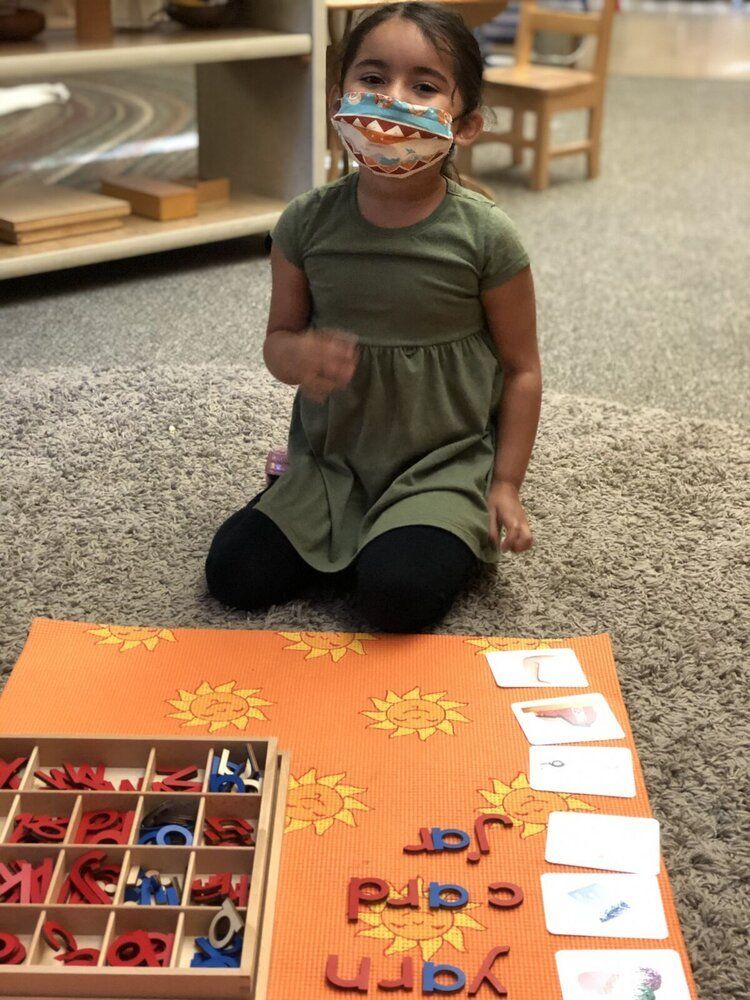 Montessori Child kneeling on carpet beside an orange alphabet matching board with cards and letter pieces.