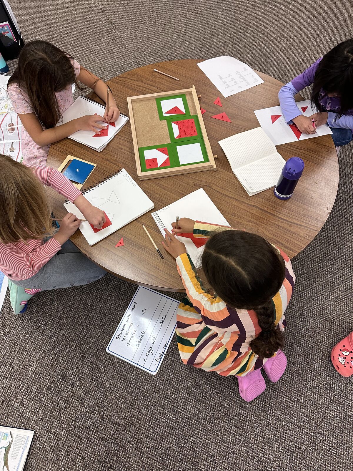 montessori Children sitting around a round table, drawing and coloring on worksheets in a classroom.