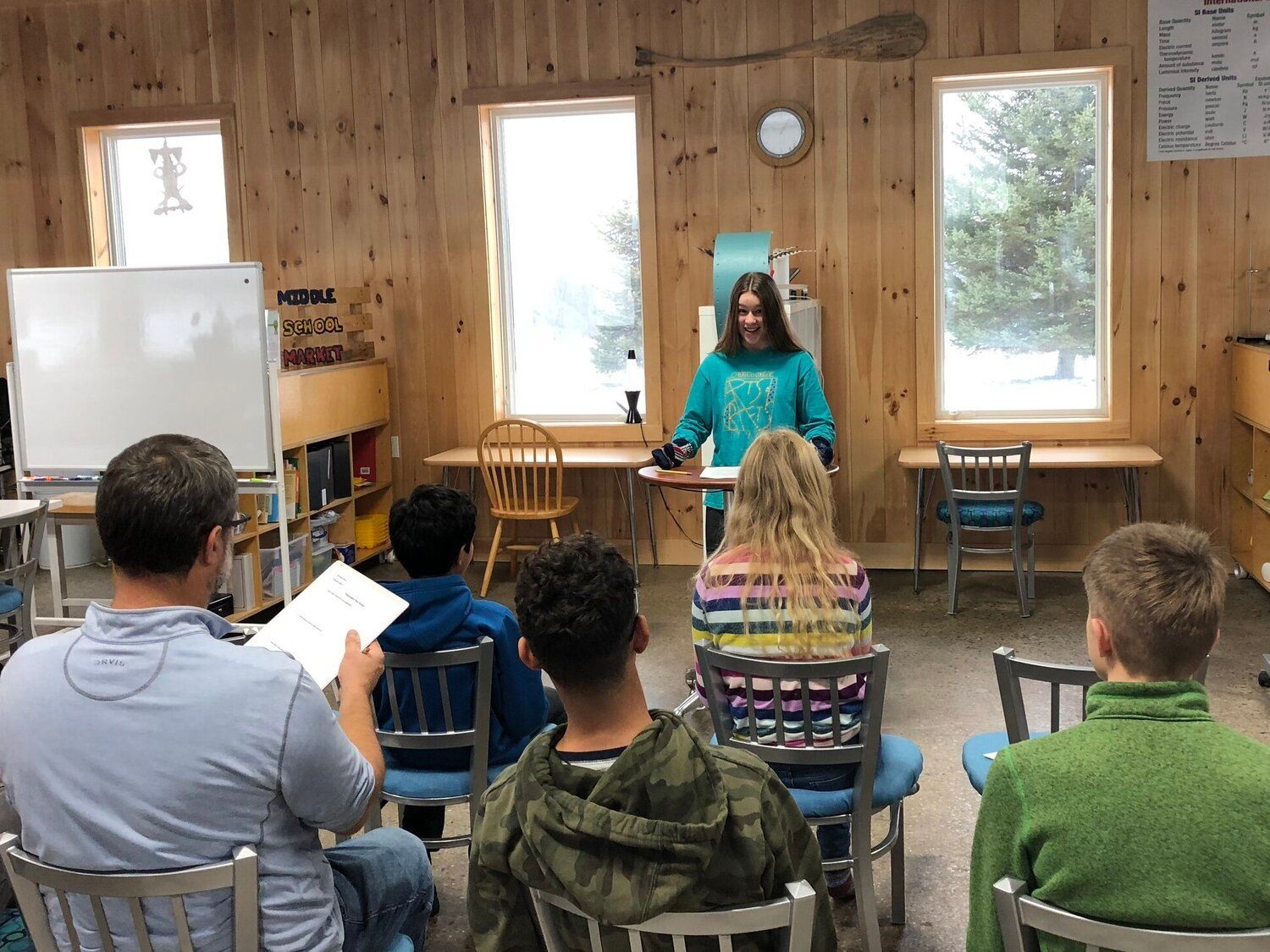 Small Montessori classroom scene with a guide at the front and seated audience in wooden room