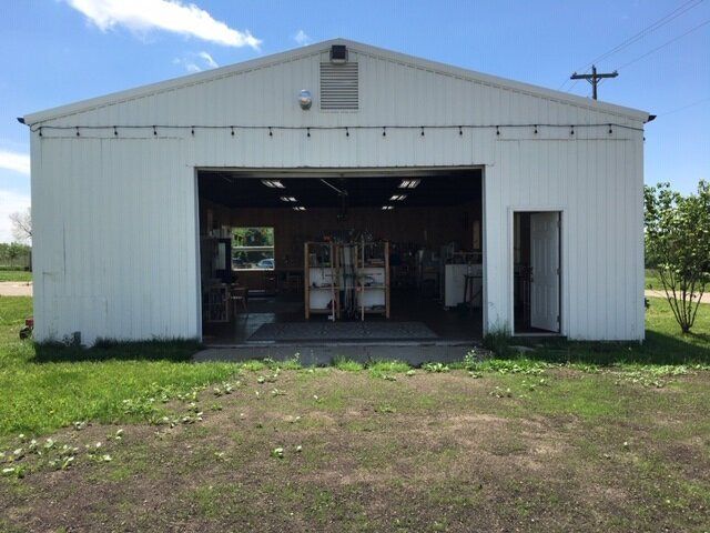 White metal warehouse with open garage door and small side entrance on a grassy lot under a blue sky