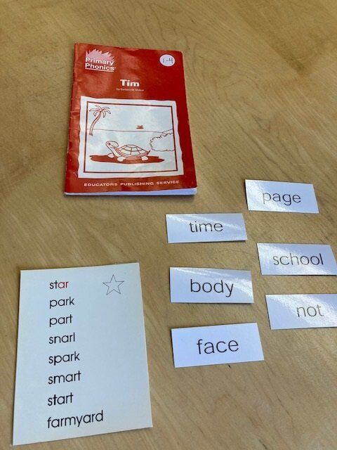 Red workbook and word cards on a wooden table, with a handwritten vocabulary list nearby.