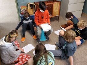 montessori Children sitting in a circle on the floor, reading papers in a classroom.