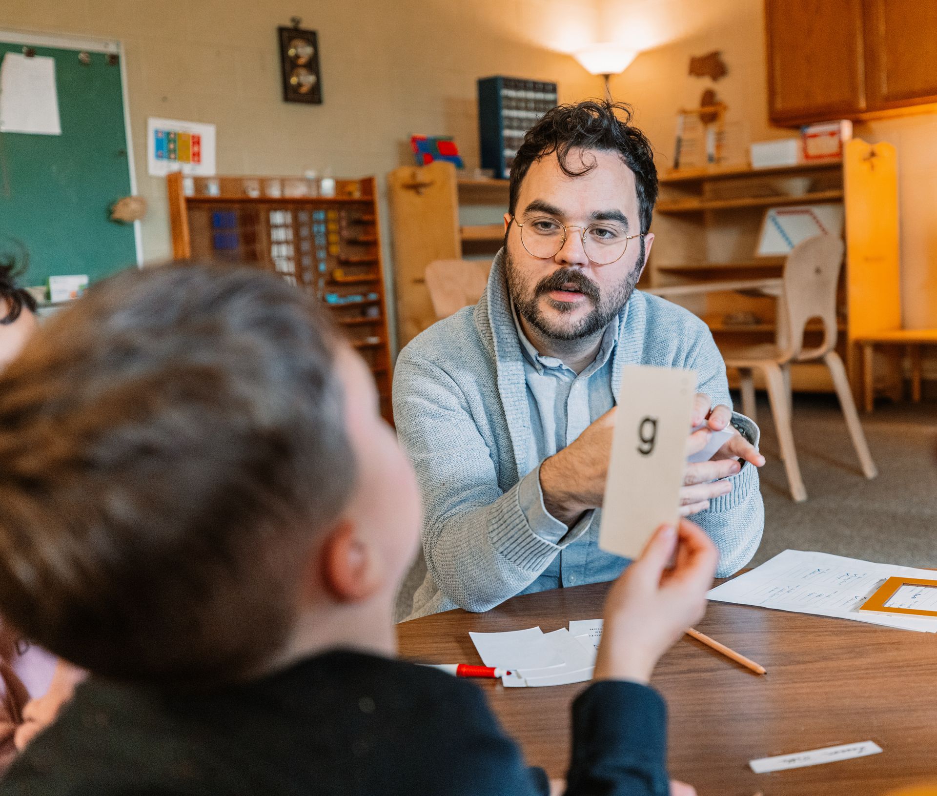 Teacher showing flashcards to a child at a table in a classroom