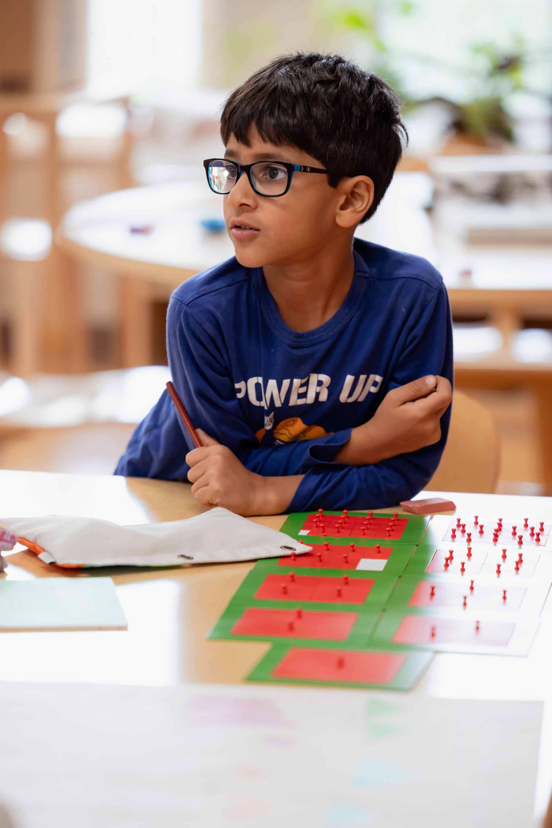 Child with glasses seated at a table with red-green fraction materials, looking to the side.