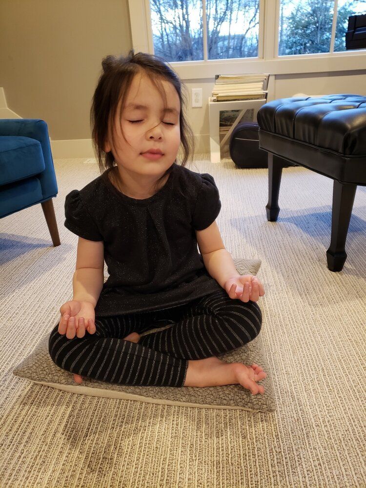 Montessori child sitting cross-legged on a carpet, eyes closed, meditating in a living room