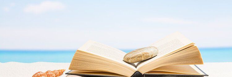 Open book with a feather quill on a beach at sunrise