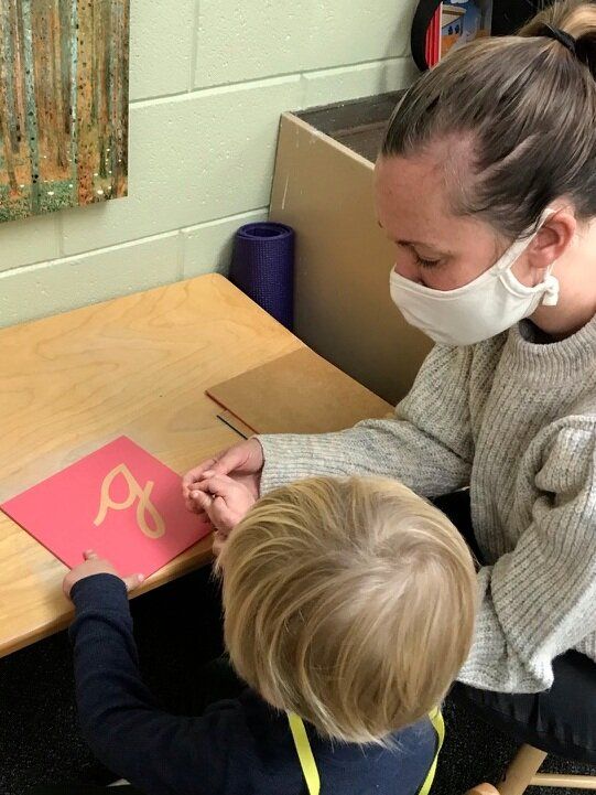 Adult and child drawing with chalk on a red board at a classroom table