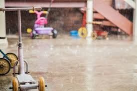 Rainy outdoor play area with a pink tricycle and scattered toys under a shelter