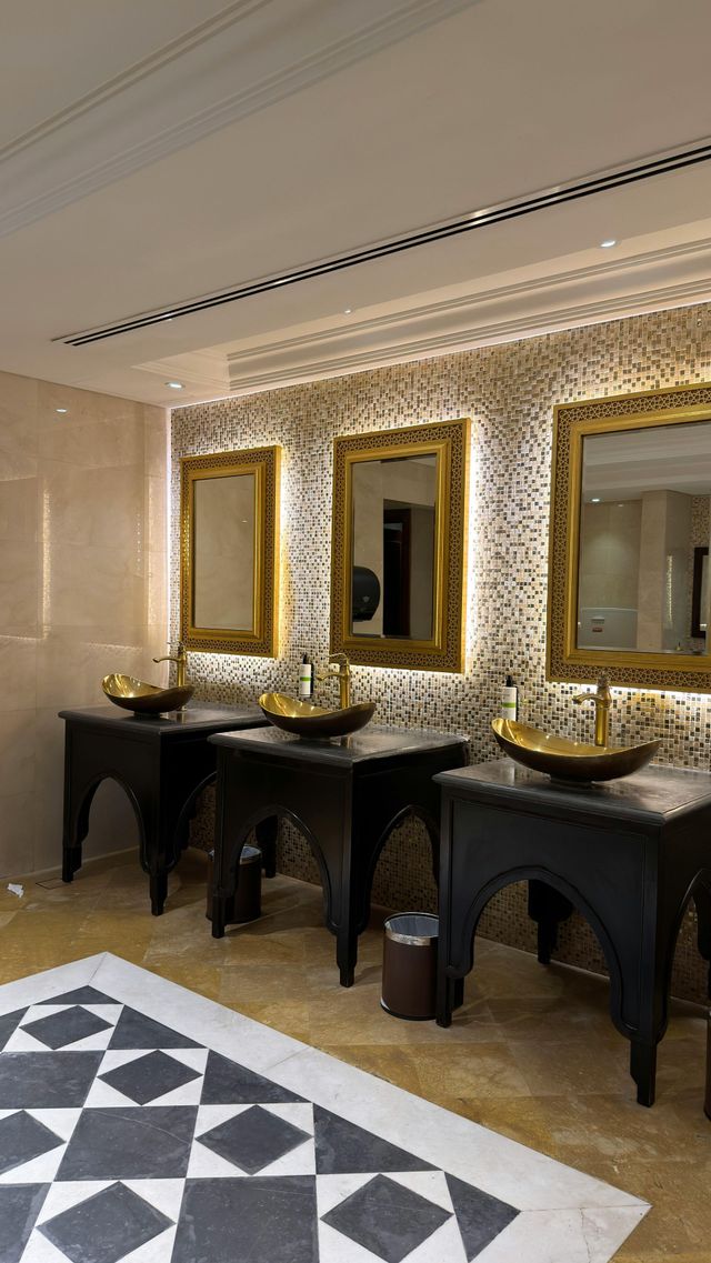Elegant restroom with gold-framed mirrors, black sinks, and patterned black-and-white floor tiles.
