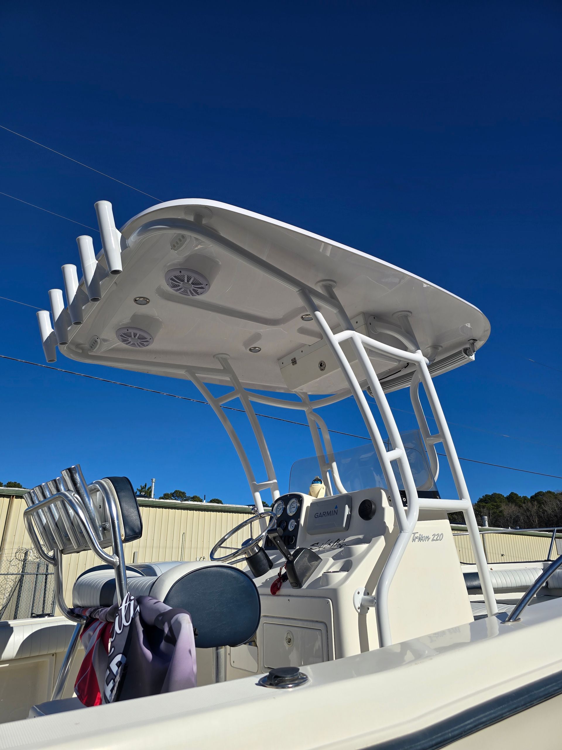 Boat cockpit under a canopy at a marina, with fishing rods and calm water at sunset.