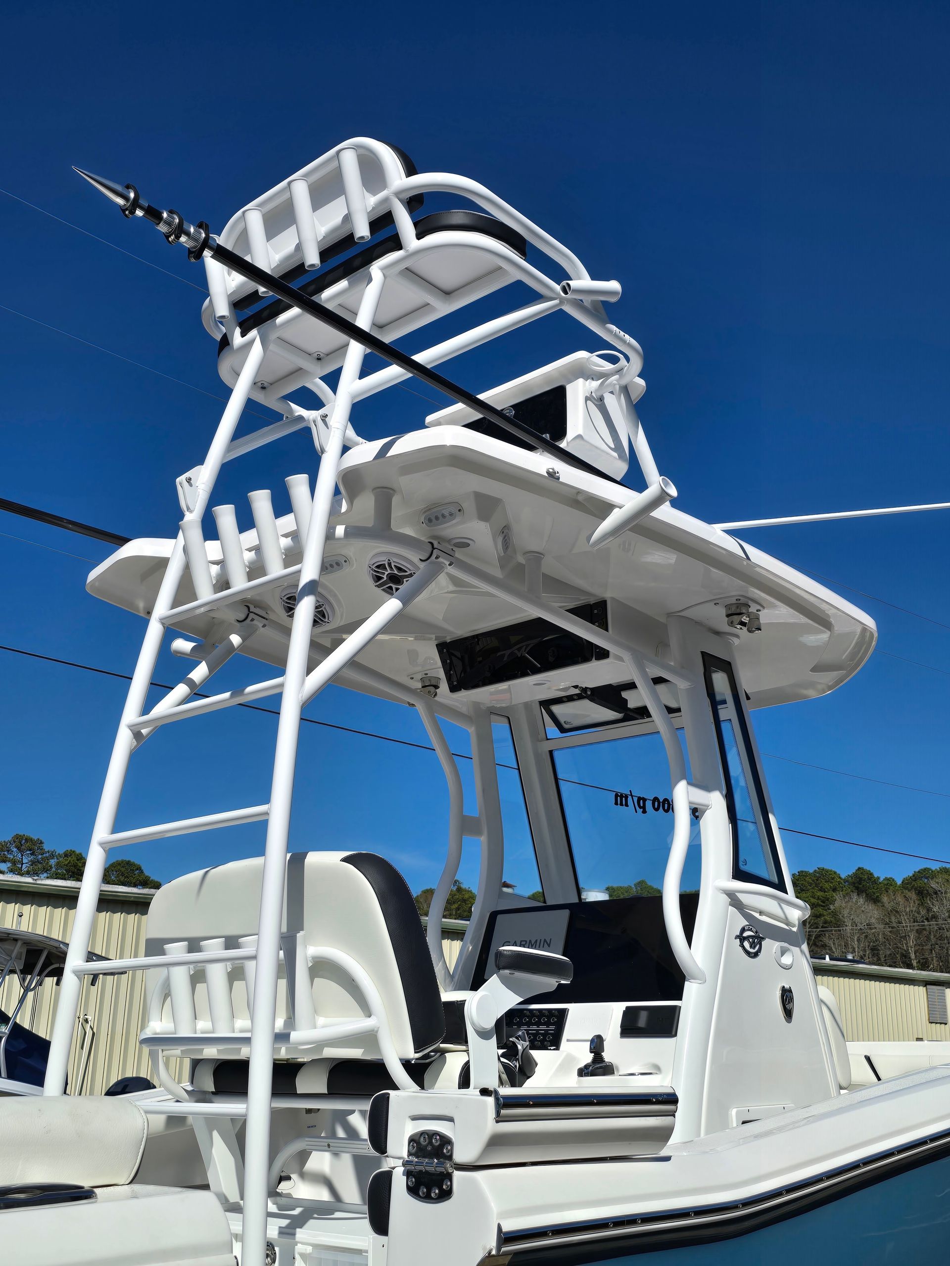 White fishing boat with a tall blue-and-white tower on calm water under a clear blue sky