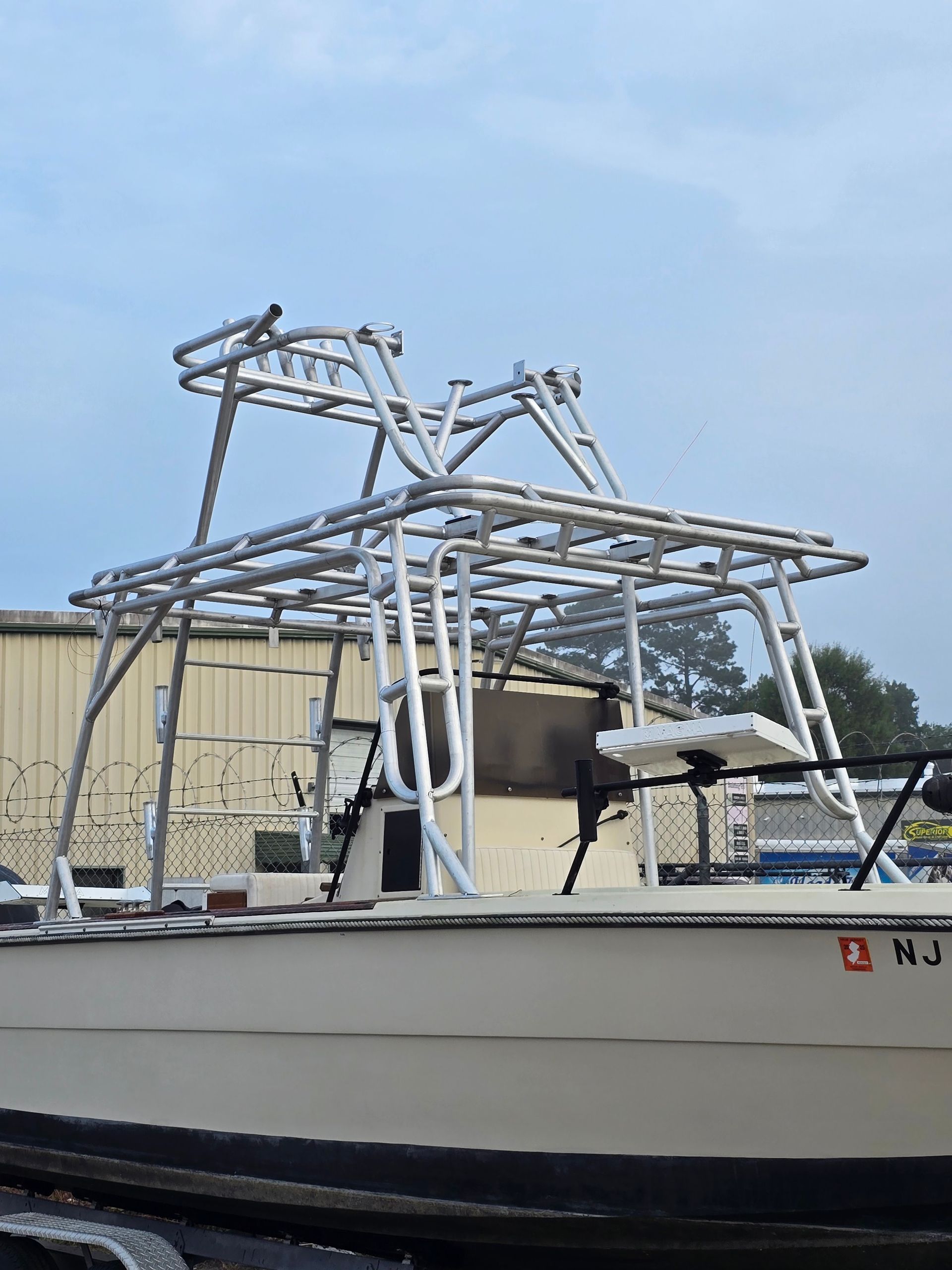 White fishing boat with metal framework on deck, moored by a beige industrial building under a blue sky