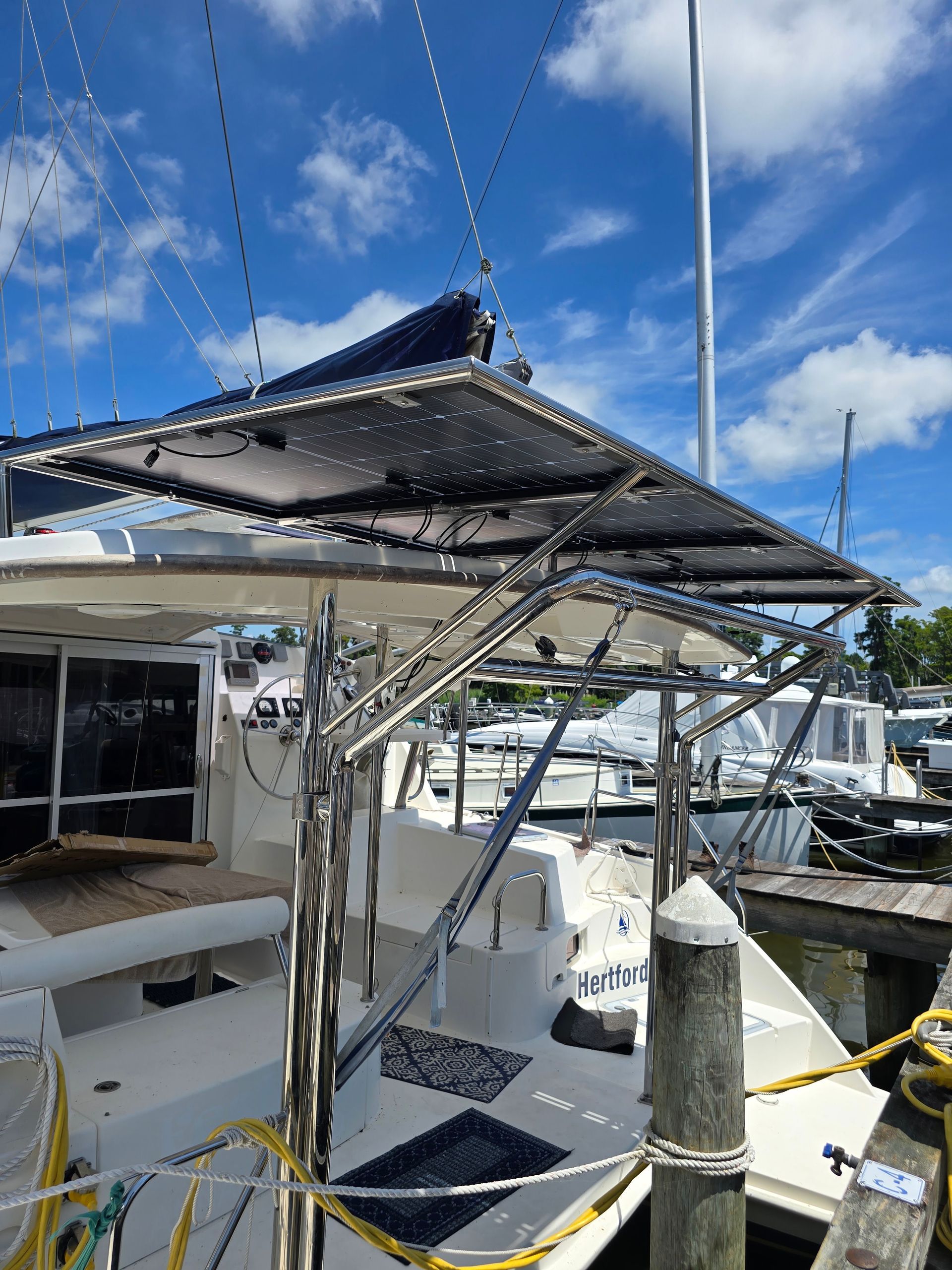 Boat dock with a black canopy, sailboat rigging, and a bright blue sky with clouds