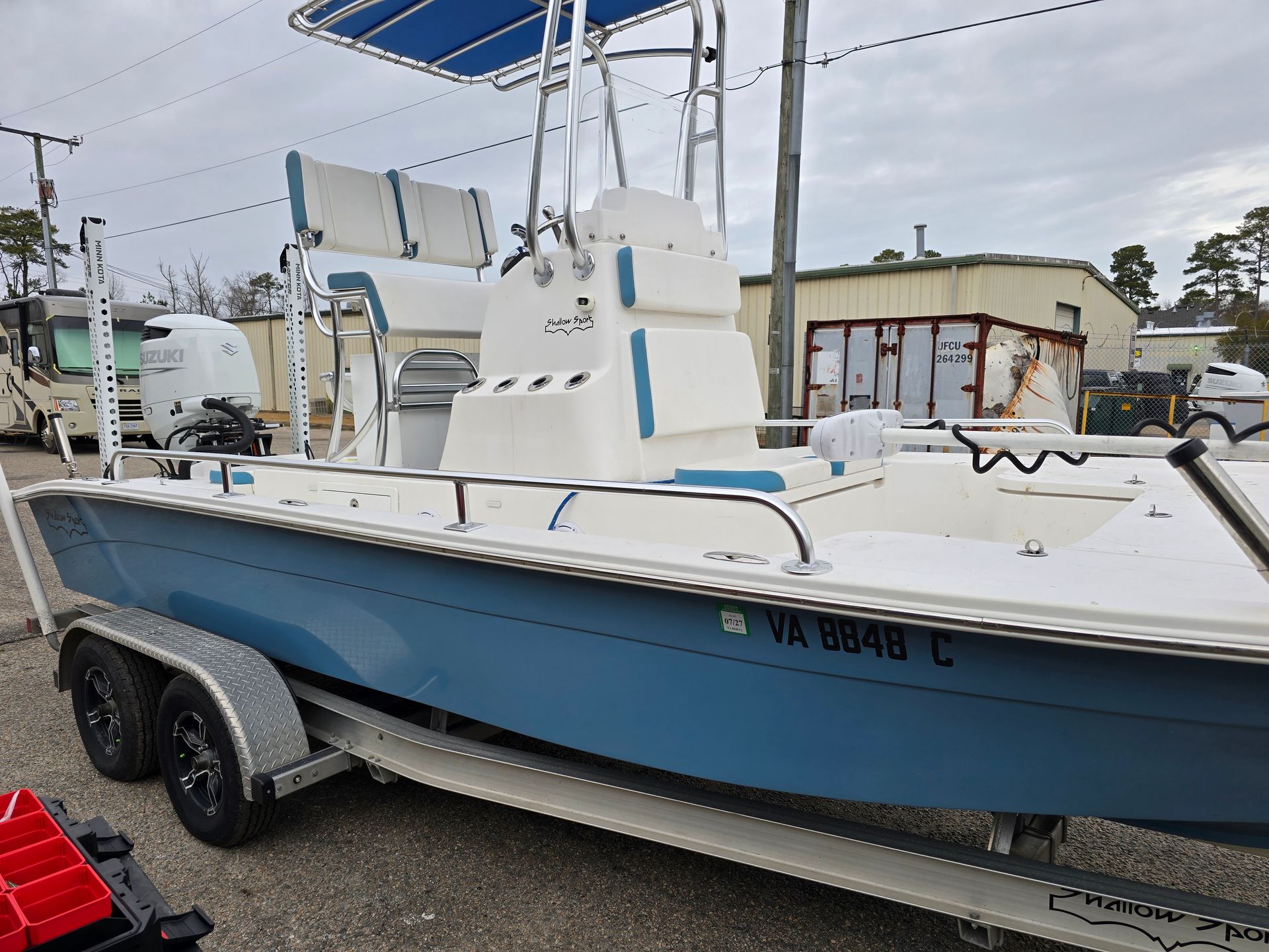 White-and-blue fishing boat on a trailer in a marina lot, with a center console and T-top.