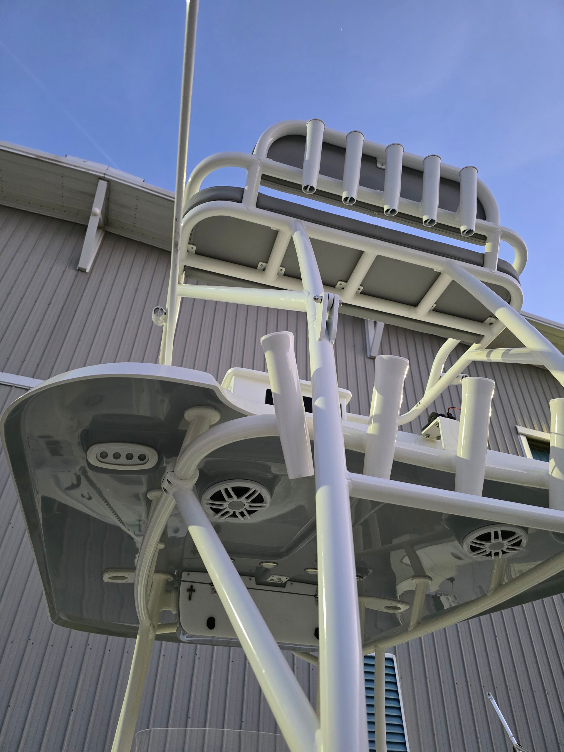 Upward view of a white steel amusement ride against a blue sky beside a building