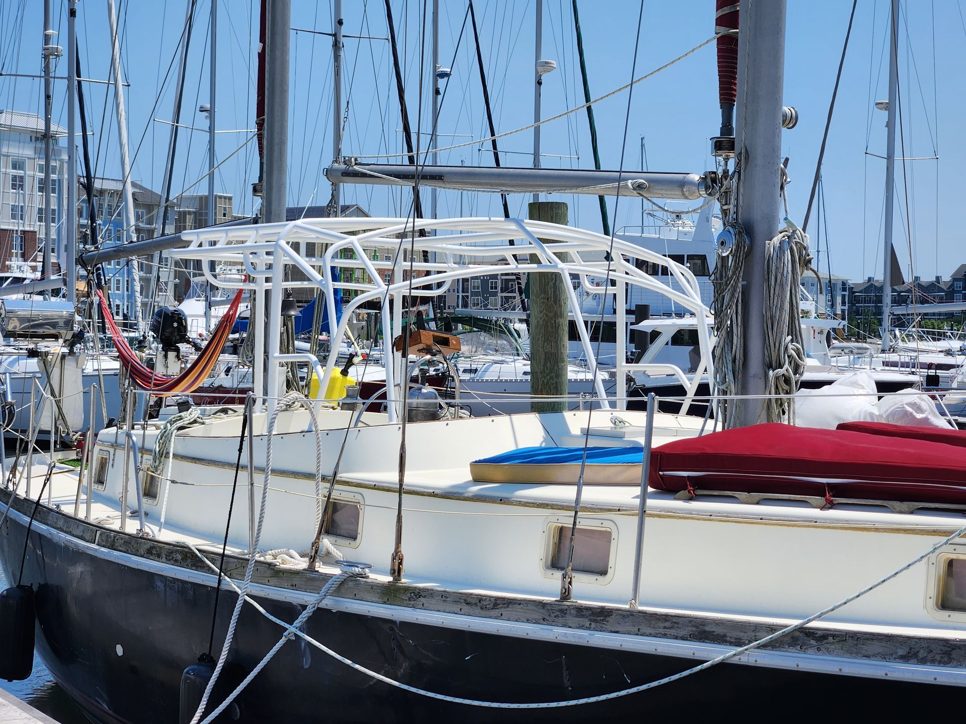 Sailboat docked at a marina with white canopy, red and blue cushions, and masts in the background