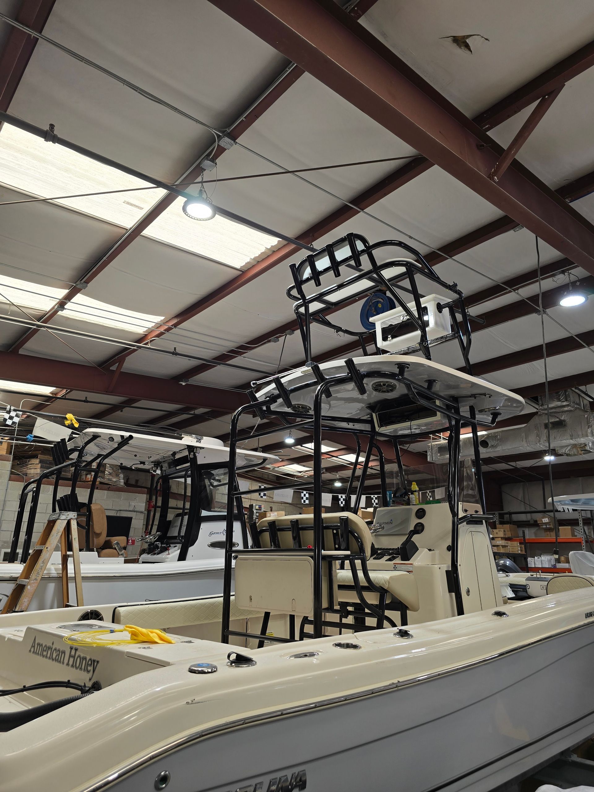 Boat under construction in a workshop, with a raised frame and overhead lights in a large warehouse.