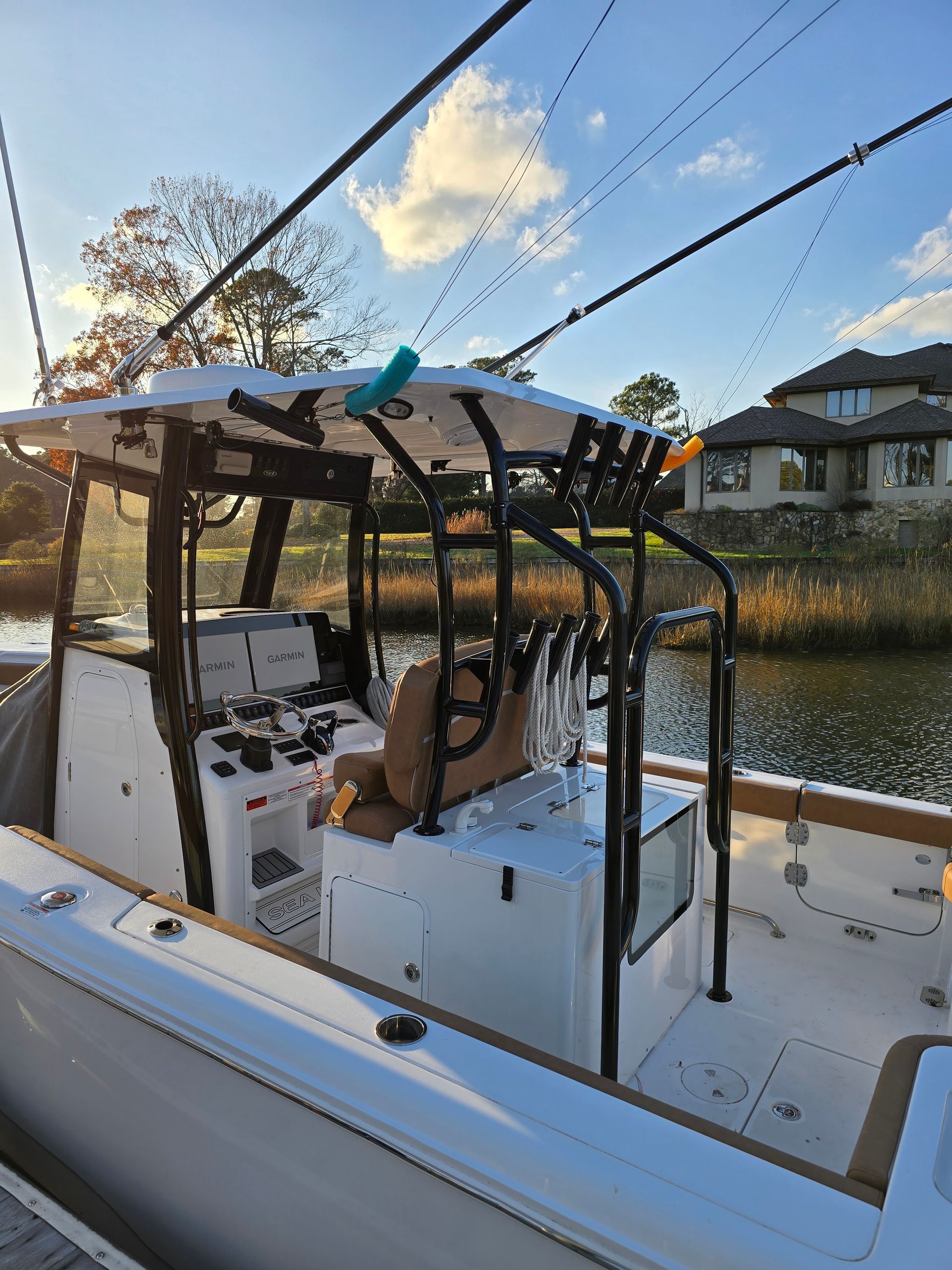 Boat cockpit under a canopy at a marina, with fishing rods and calm water at sunset.