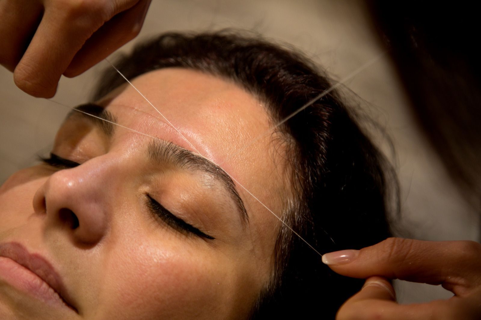 Person getting eyebrows threaded with white thread in a salon.