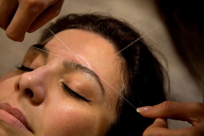 Person getting eyebrows threaded with white thread in a salon.