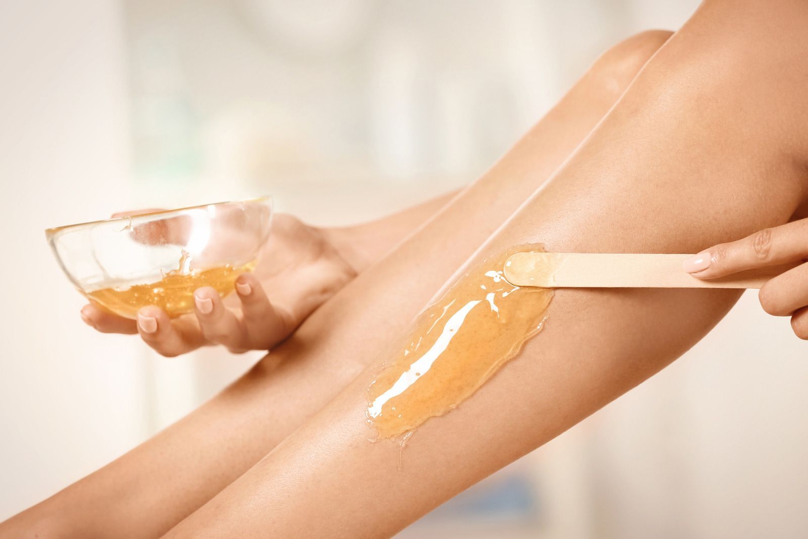 Person applying hair removal wax to their leg with a wooden applicator.