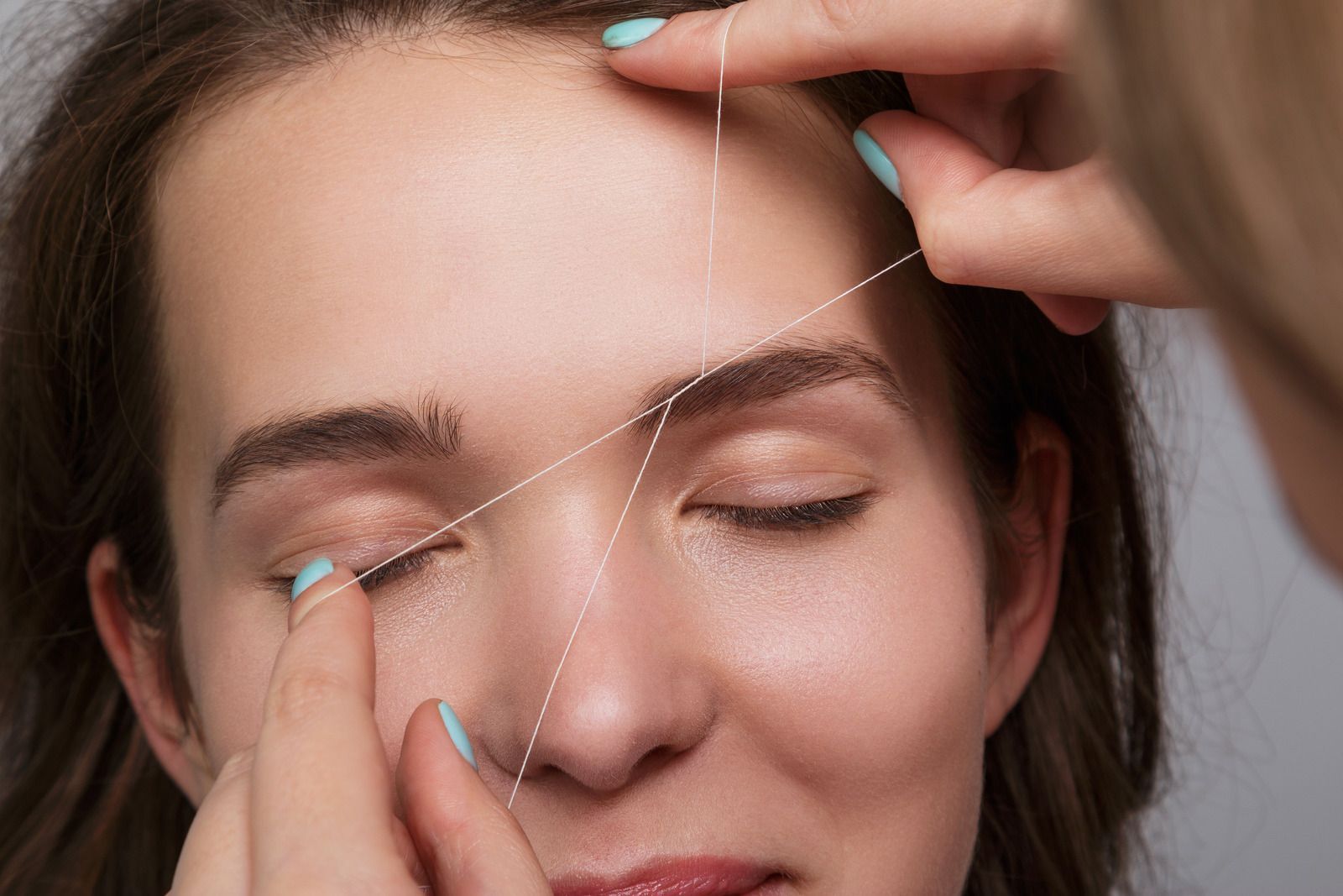 Person getting eyebrow threading with cotton thread.
