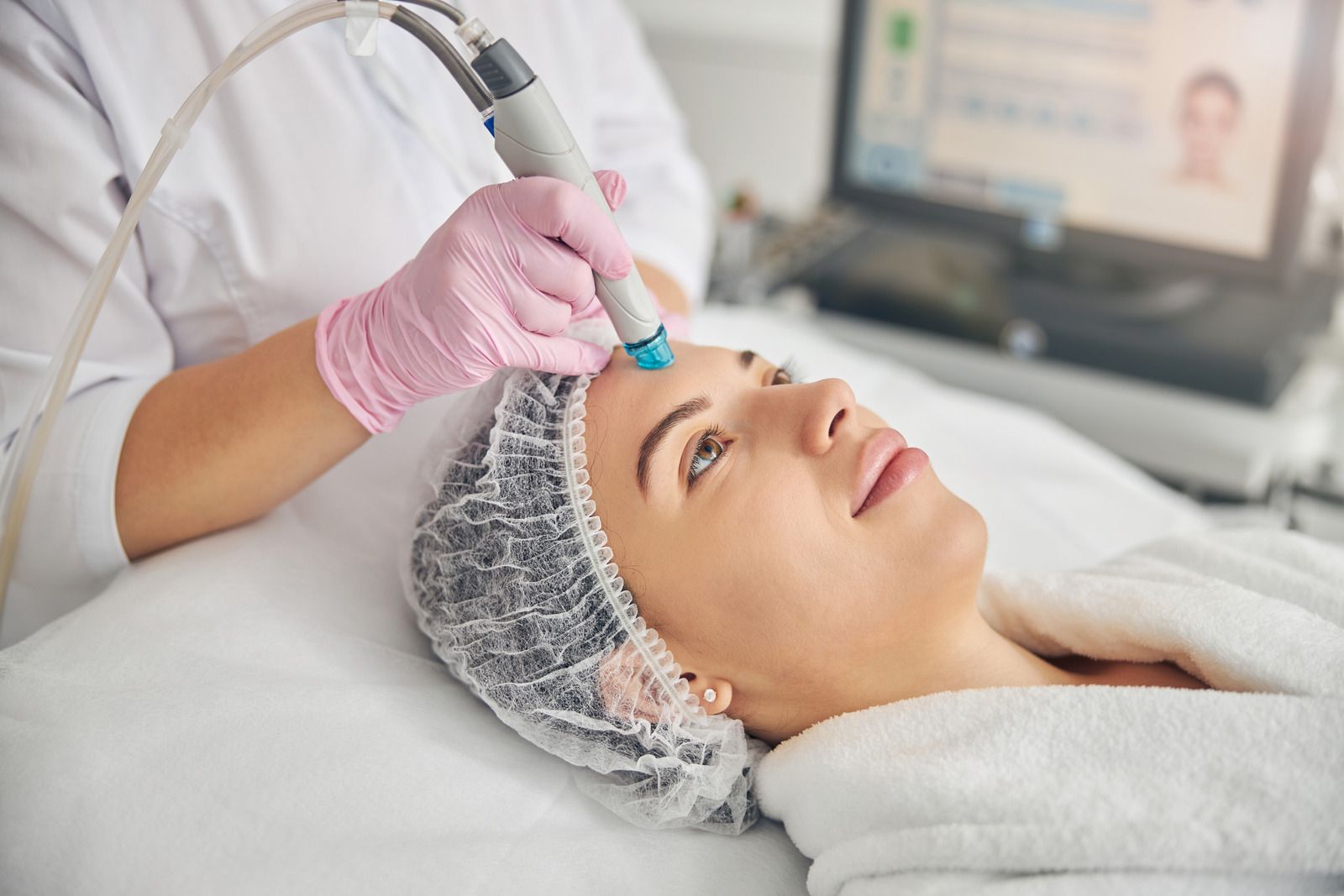 Woman receiving facial treatment in a salon. Therapist with pink gloves, using a handheld device.