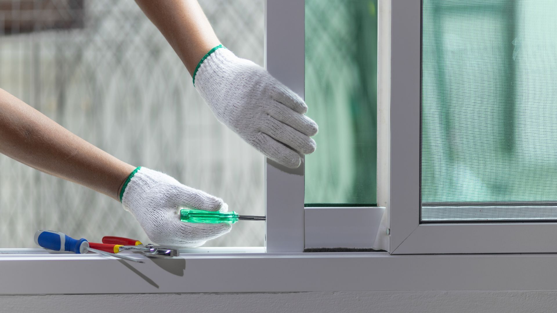 A person is fixing a sliding glass door with a screwdriver.