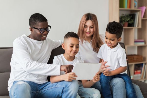 Four people on a couch look at a tablet together in a bright living room.