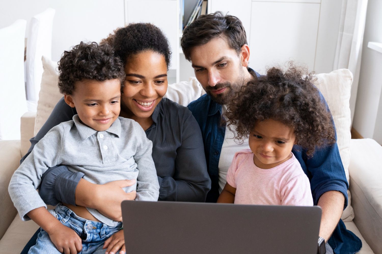 Family gathered on a couch, smiling and looking at a laptop together