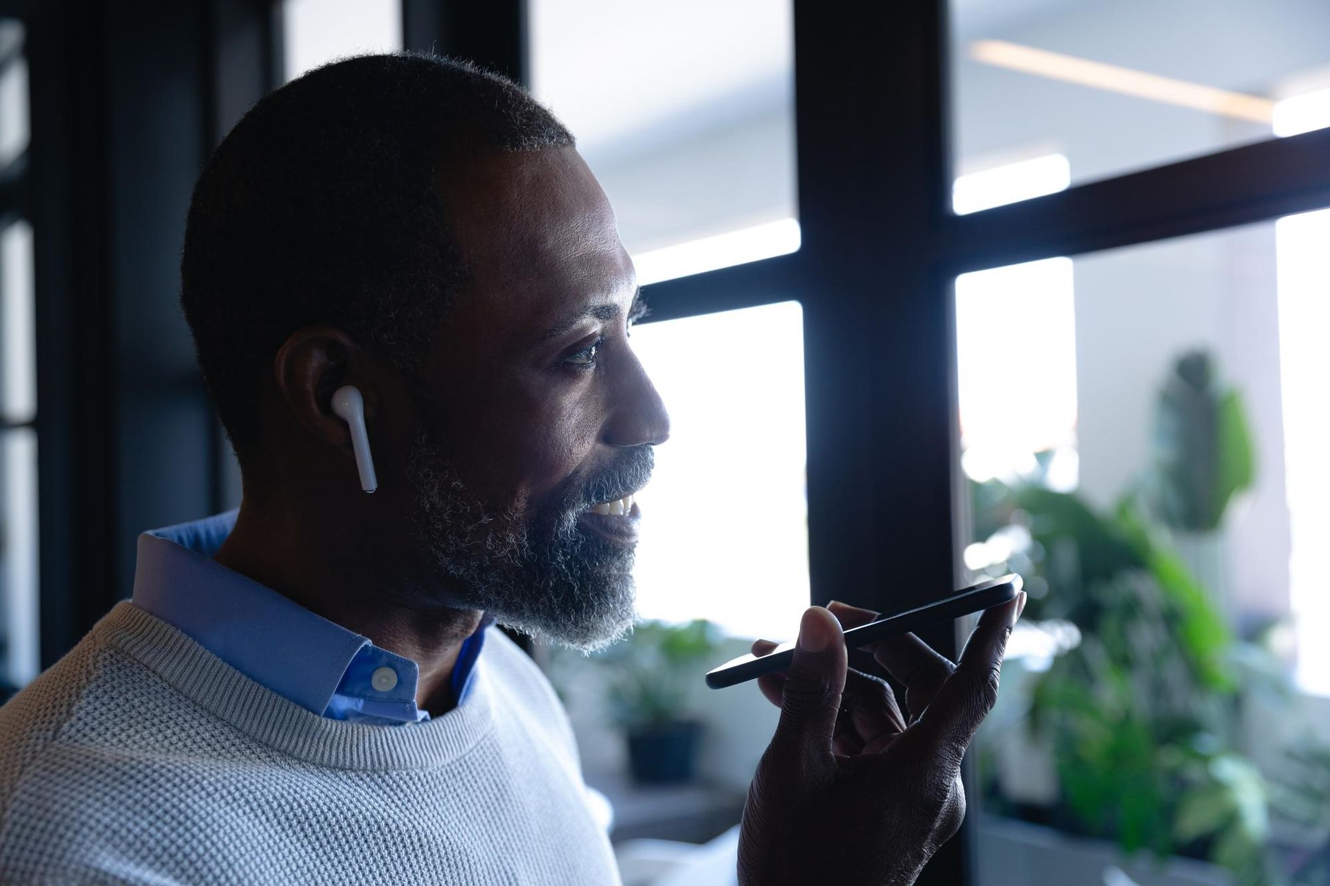 Person speaking into a smartphone near a window, with indoor plants in the background