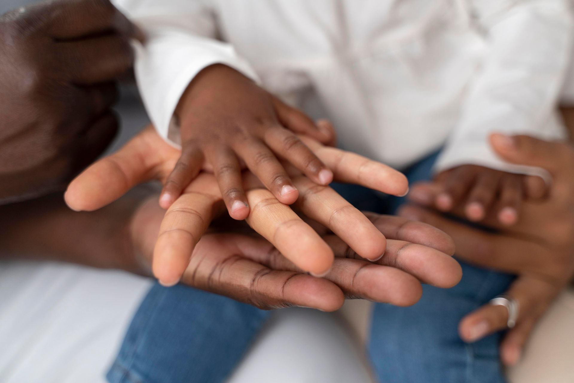 Hands of adults and a child stacked together in a close-up on a couch