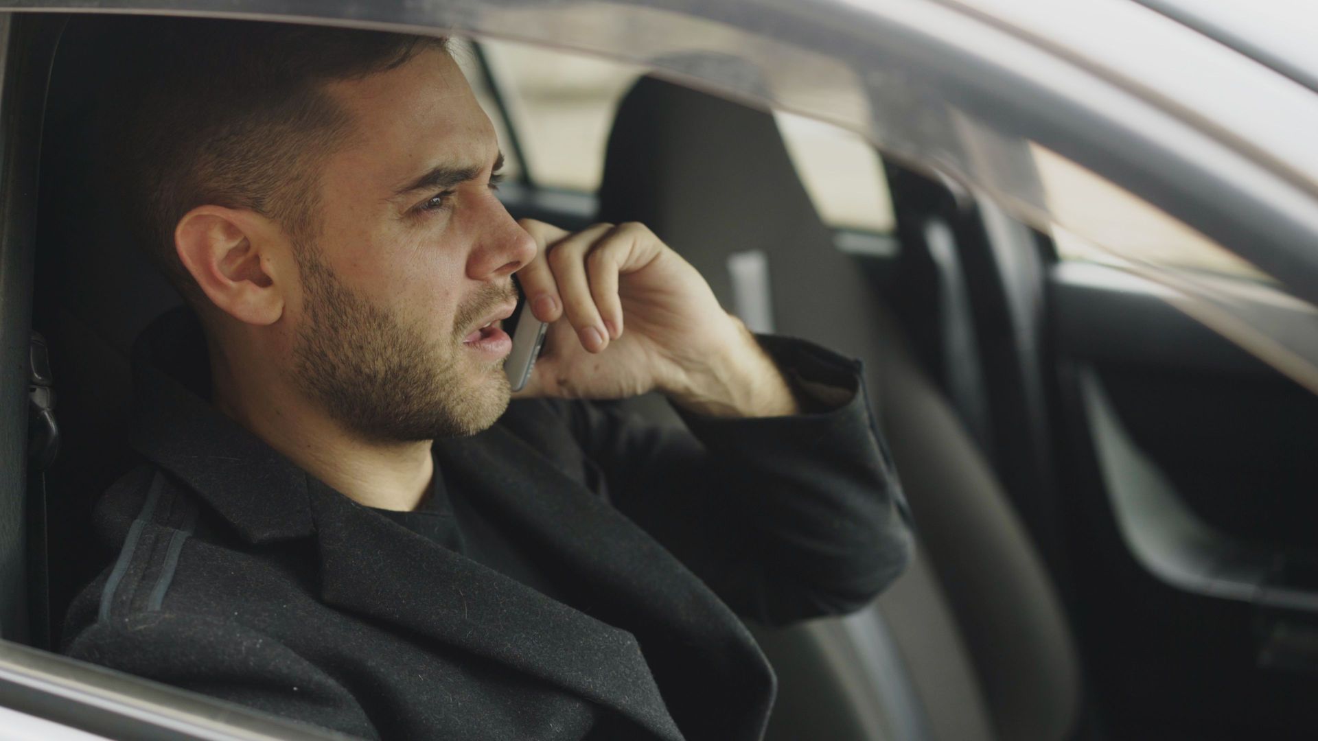 Man sitting in a car, talking on a phone with a serious expression