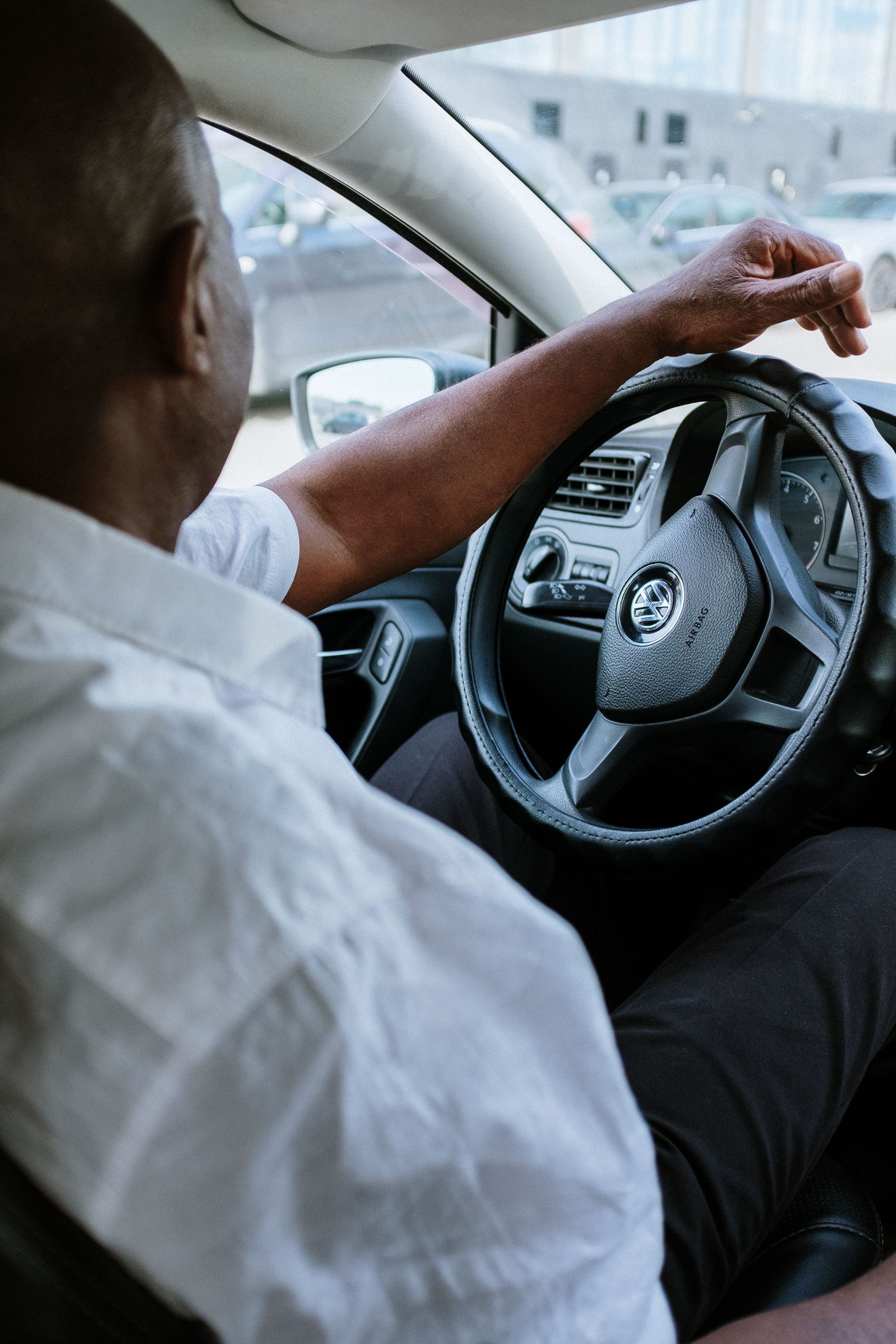 Driver in a white shirt steering a car, viewed from the back seat.