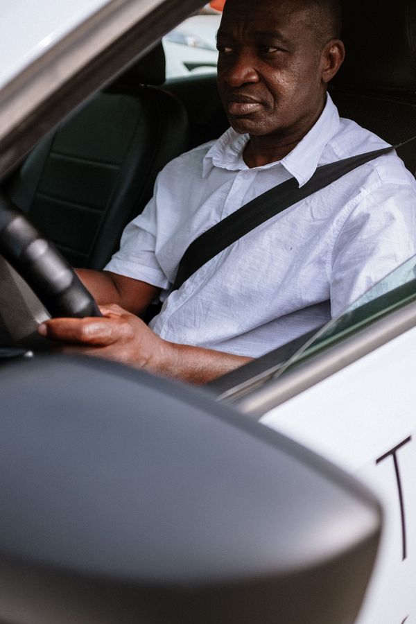 Man sitting in the driver’s seat of a car, wearing a white shirt and seat belt, hands on the wheel.