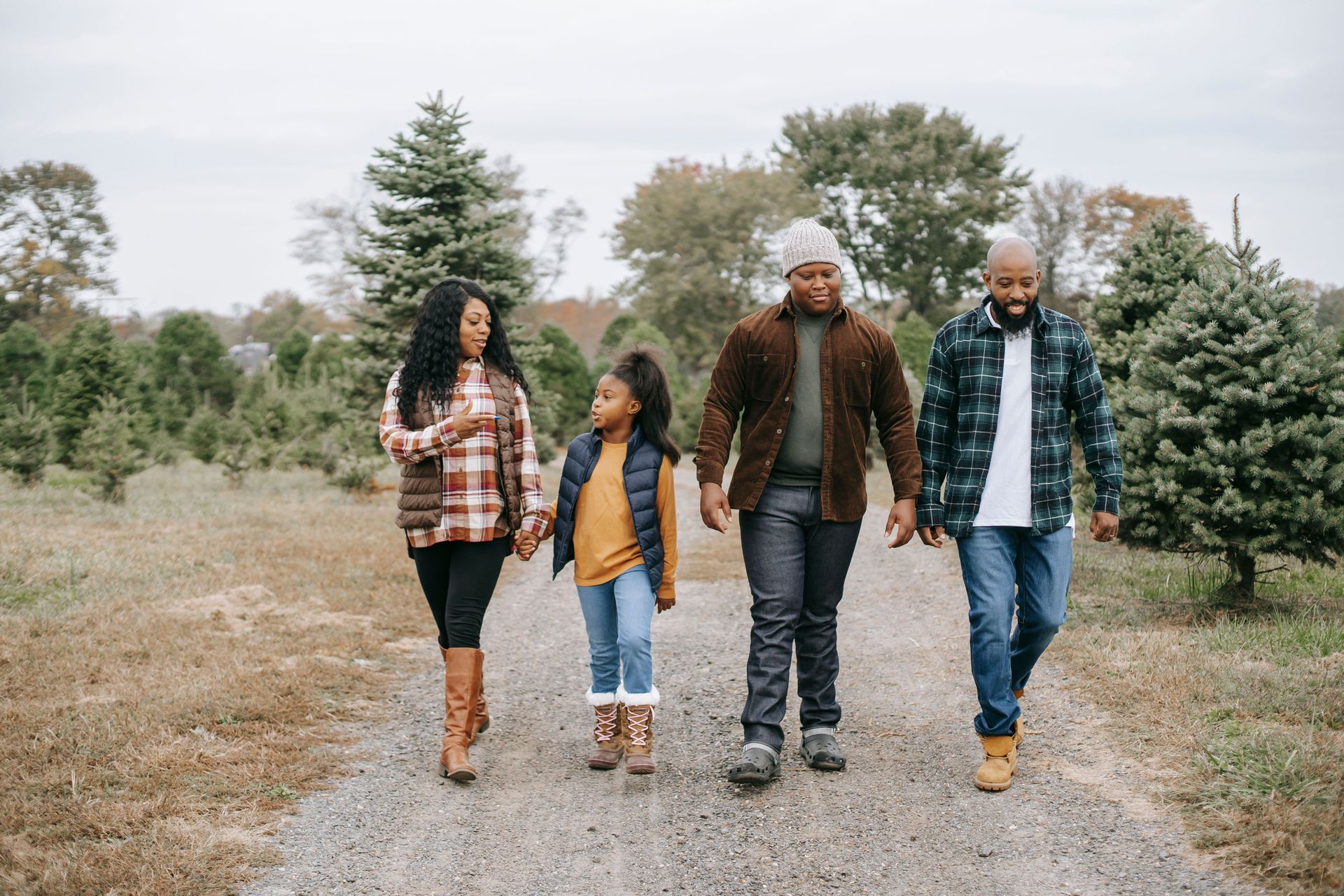 Four people walking on a gravel path through a rural field with evergreen trees.