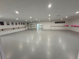 Empty dance studio with mirrors, ballet barres, and gray floor.