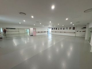 Empty dance studio with mirrors, barre, and gray floor.