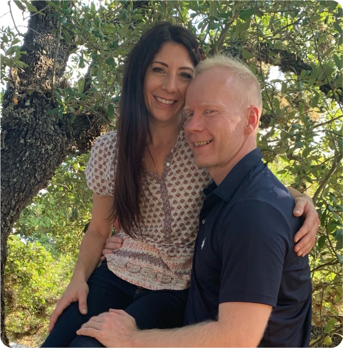 A man and a woman are posing for a picture under a tree
