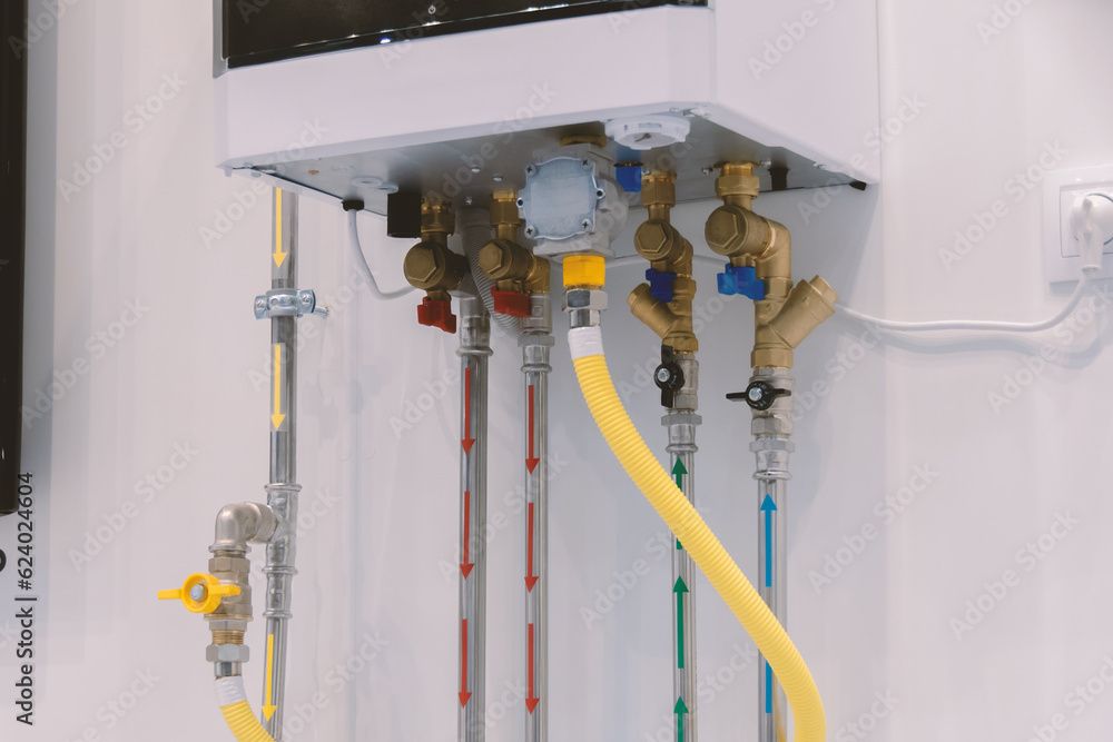 Plumbing pipes connected to a white wall-mounted boiler with yellow and blue pipes and brass valves.
