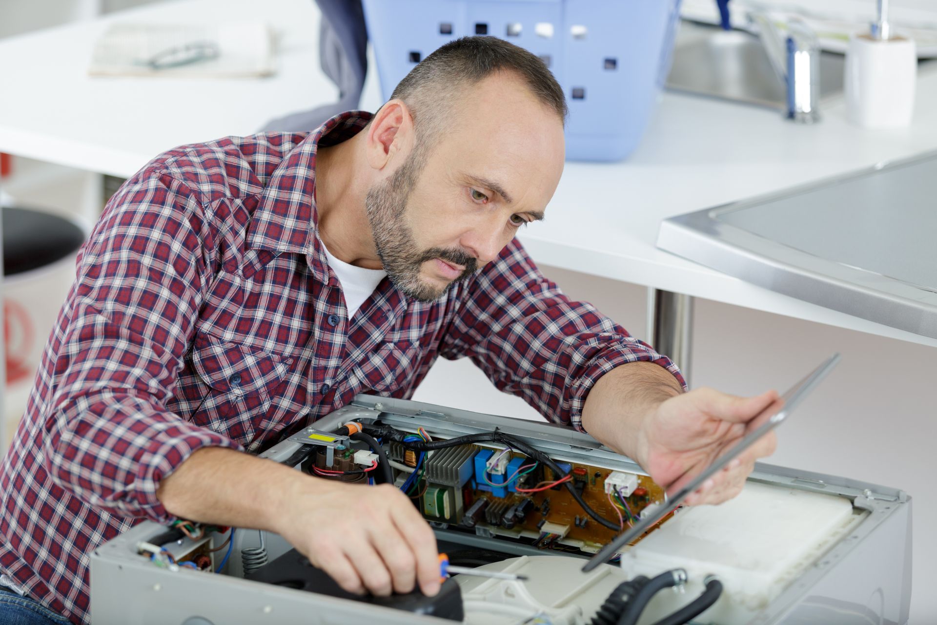 Man in plaid shirt repairs appliance, working on internal components.