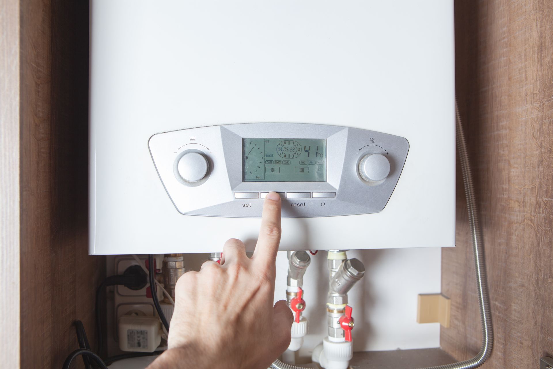 A person's hand pressing a button on a white wall-mounted boiler with a digital display.