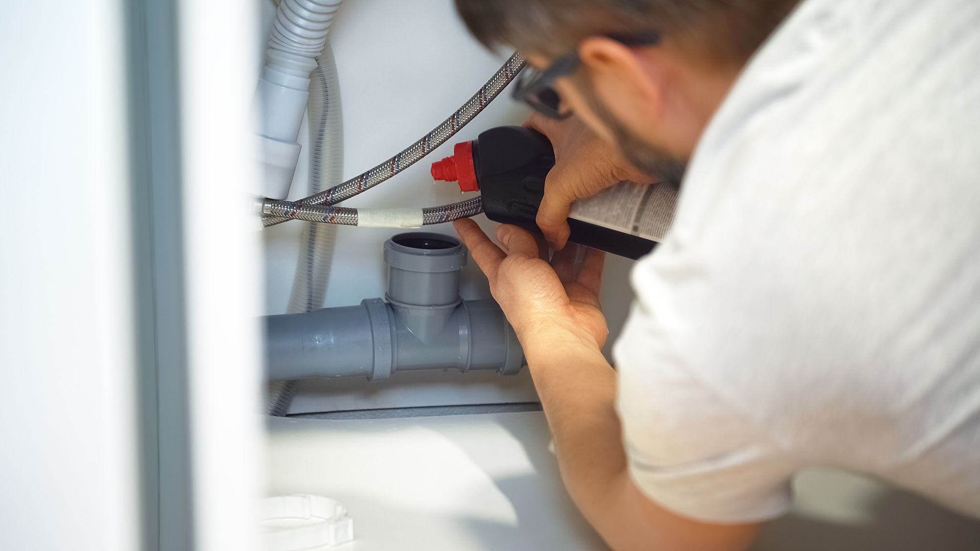 Person working on plumbing under a sink, using a tool on a pipe.
